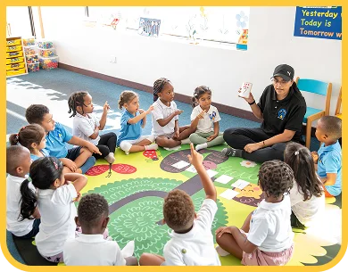 An educator leading a group activity with children seated on the mat